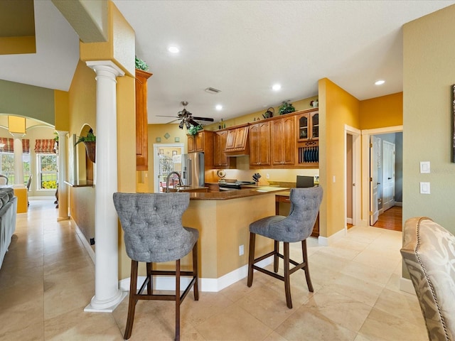 kitchen featuring appliances with stainless steel finishes, a kitchen bar, decorative columns, kitchen peninsula, and ceiling fan