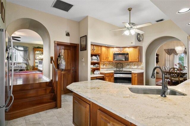 kitchen featuring sink, backsplash, appliances with stainless steel finishes, light stone countertops, and ceiling fan