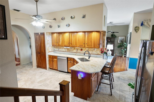 kitchen featuring decorative backsplash, a breakfast bar, stainless steel appliances, ceiling fan, and sink