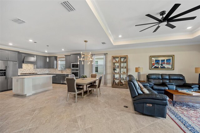 living room with ceiling fan with notable chandelier, ornamental molding, and a tray ceiling