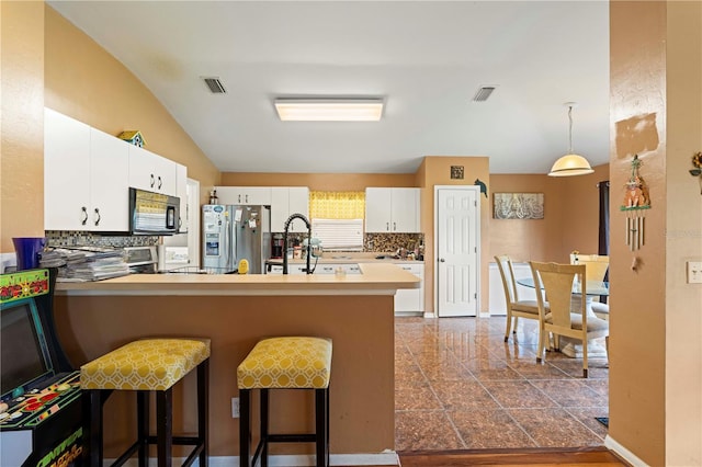 kitchen with light tile patterned floors, stainless steel fridge, kitchen peninsula, a kitchen breakfast bar, and tasteful backsplash