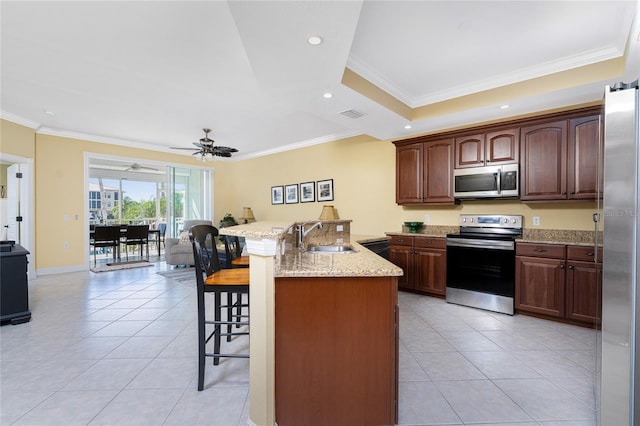 kitchen with light stone countertops, stainless steel appliances, sink, ceiling fan, and a kitchen bar