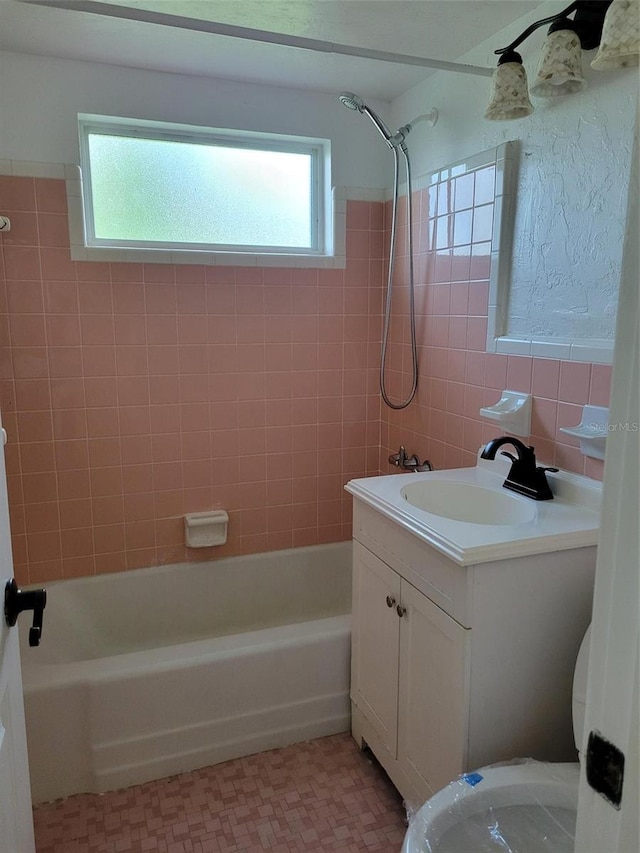 full bathroom with tile walls, toilet, tiled shower / bath combo, and vanity