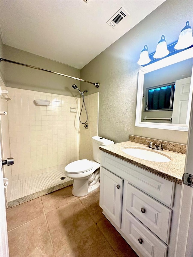 bathroom with vanity, toilet, a tile shower, and tile patterned floors