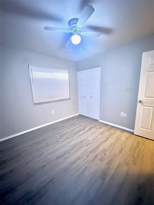 unfurnished bedroom with a closet, baseboards, wood finished floors, and a ceiling fan