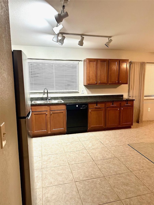 kitchen featuring a sink, black dishwasher, freestanding refrigerator, brown cabinetry, and light tile patterned floors