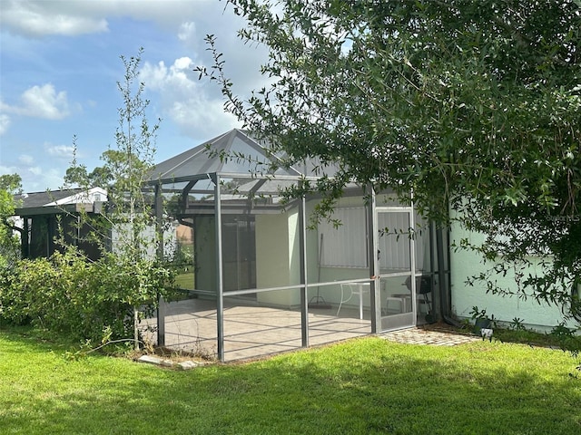 back of house featuring a yard, glass enclosure, and a patio