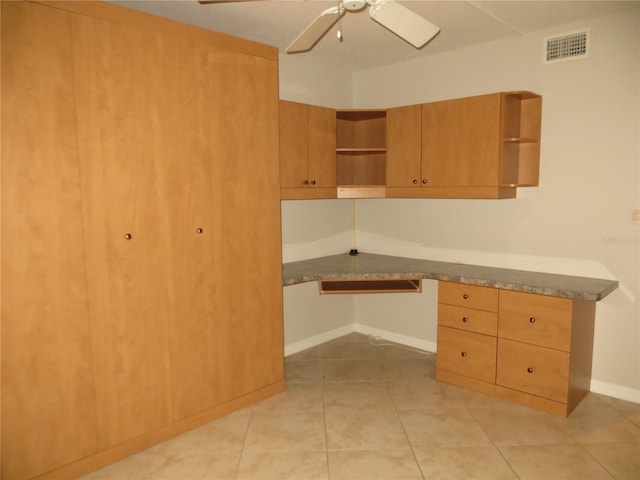 unfurnished office featuring ceiling fan, light tile patterned flooring, and built in desk