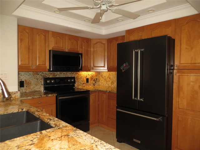 kitchen with light stone countertops, a raised ceiling, sink, black appliances, and light tile patterned floors