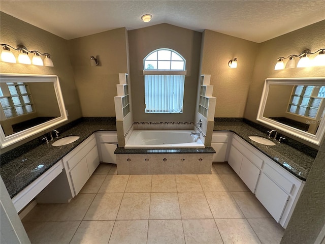 bathroom featuring a textured ceiling, vanity, vaulted ceiling, tile patterned floors, and tiled tub