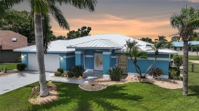 view of front of home featuring metal roof, an attached garage, fence, a yard, and stucco siding