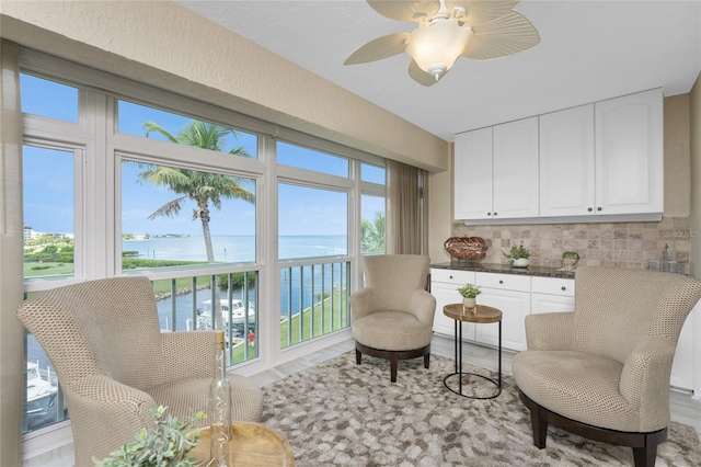 sitting room with a water view, light hardwood / wood-style flooring, ceiling fan, and a wealth of natural light