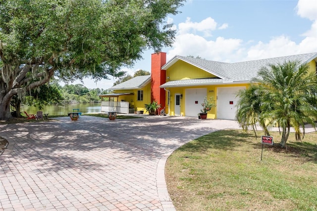 view of front of home featuring a chimney, an attached garage, a water view, decorative driveway, and a front lawn