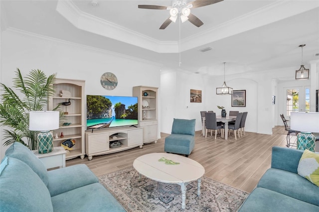 living room with light wood finished floors, ornamental molding, and a raised ceiling