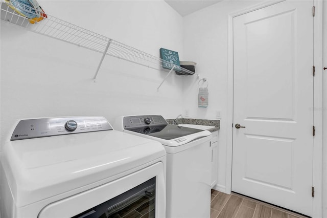 washroom featuring wood finish floors, cabinet space, a sink, and separate washer and dryer