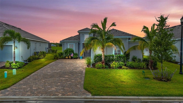 view of front of house with stucco siding, decorative driveway, and a yard