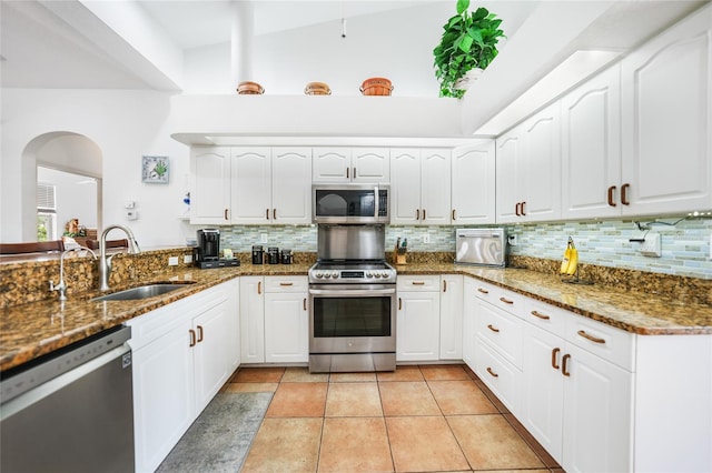 kitchen featuring tasteful backsplash, stainless steel appliances, sink, lofted ceiling, and dark stone counters