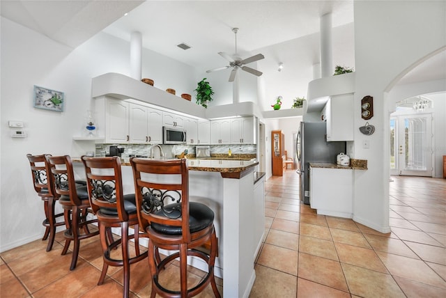 kitchen featuring stainless steel appliances, ceiling fan, a kitchen breakfast bar, kitchen peninsula, and high vaulted ceiling