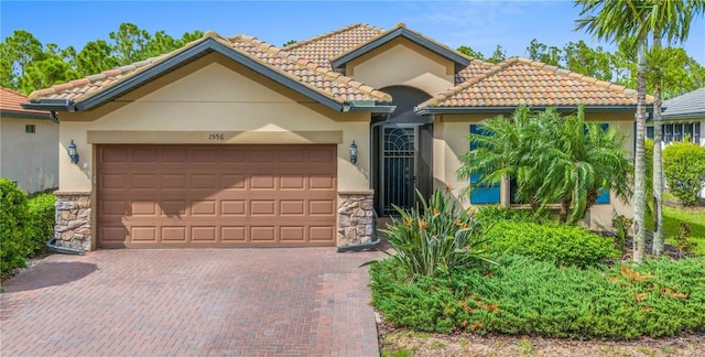 mediterranean / spanish home with an attached garage, stone siding, a tiled roof, decorative driveway, and stucco siding