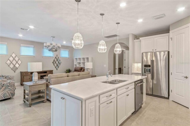 kitchen with a center island with sink, appliances with stainless steel finishes, hanging light fixtures, sink, and white cabinetry