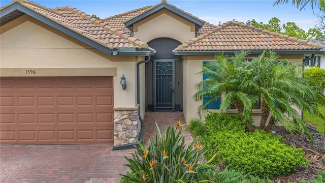 view of front facade with stone siding, a tiled roof, an attached garage, decorative driveway, and stucco siding