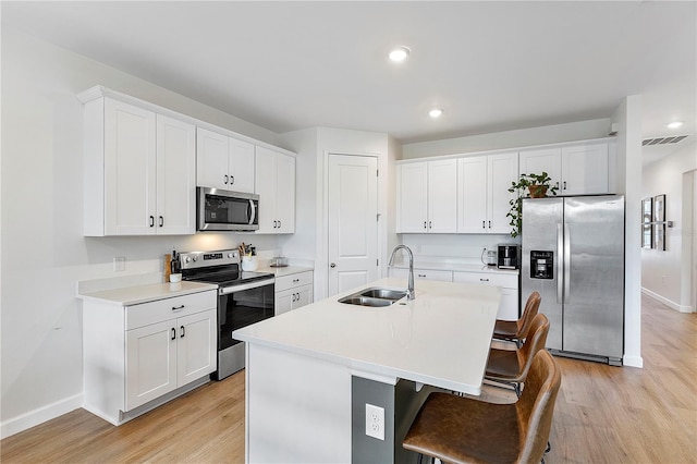 kitchen with white cabinets, stainless steel appliances, light hardwood / wood-style floors, sink, and a kitchen island with sink