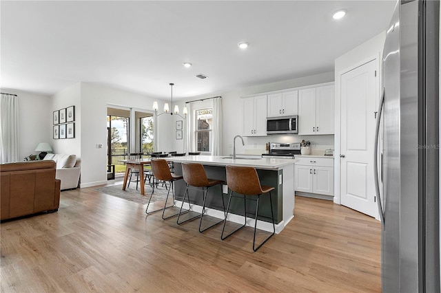 kitchen featuring a center island with sink, light hardwood / wood-style flooring, stainless steel appliances, and white cabinets