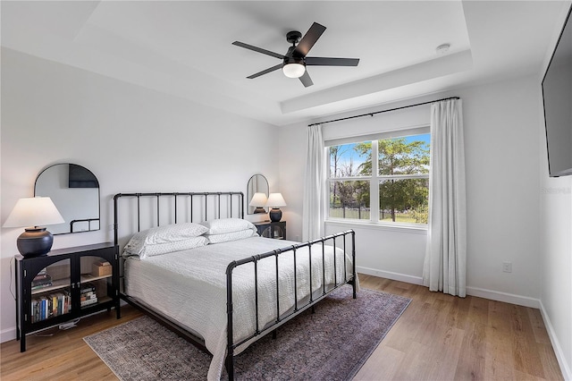 bedroom with a raised ceiling, ceiling fan, and light hardwood / wood-style floors