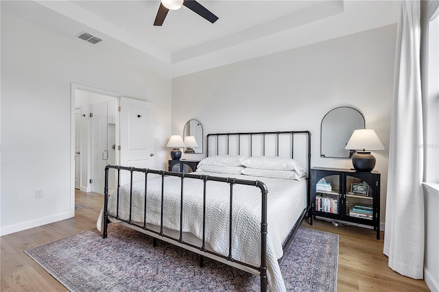 bedroom with a raised ceiling, hardwood / wood-style floors, and ceiling fan