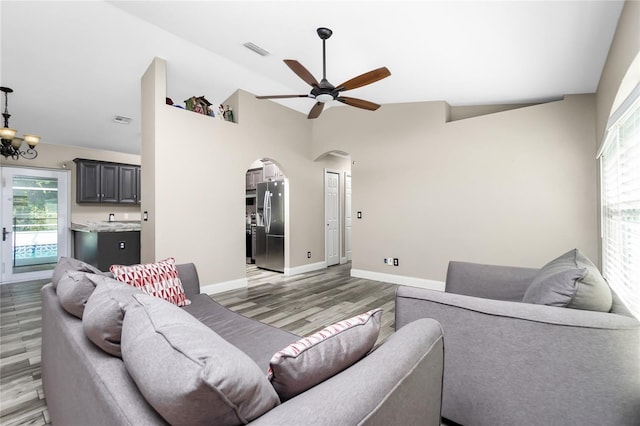 living room with ceiling fan with notable chandelier, light hardwood / wood-style floors, and vaulted ceiling