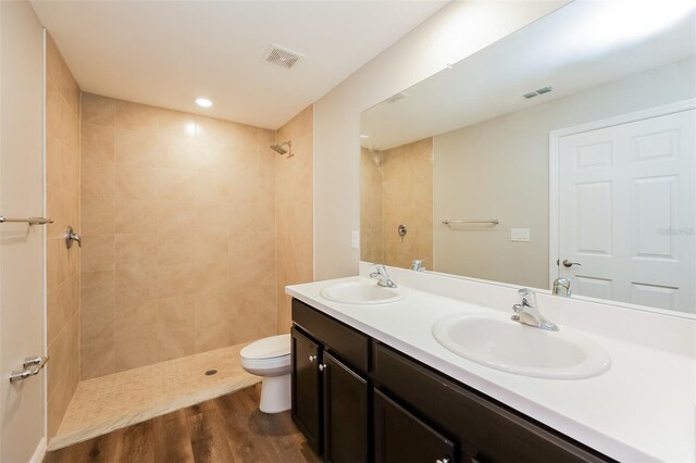 bathroom with vanity, toilet, hardwood / wood-style floors, and tiled shower