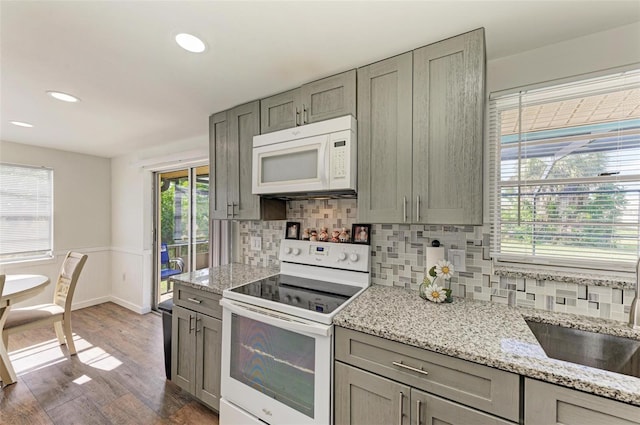 kitchen featuring decorative backsplash, white appliances, light stone counters, and dark wood-type flooring