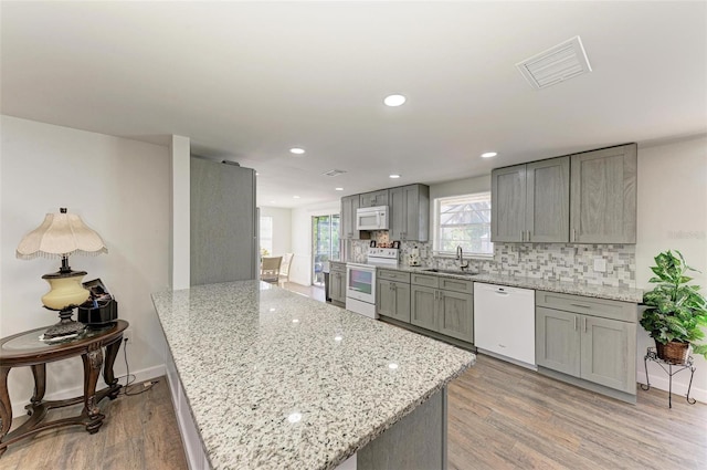 kitchen featuring light stone countertops, sink, kitchen peninsula, light hardwood / wood-style floors, and white appliances