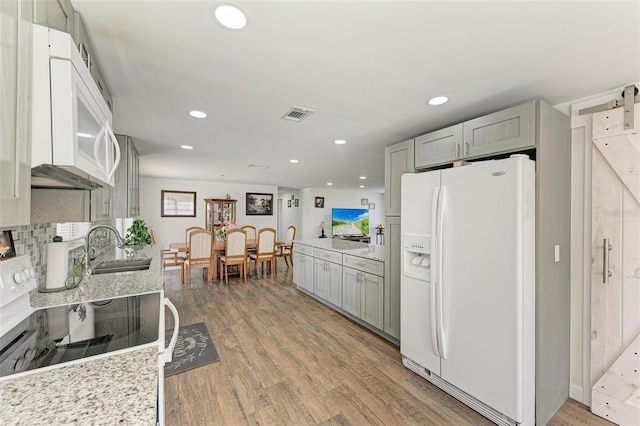 kitchen with gray cabinetry, white appliances, sink, hardwood / wood-style flooring, and a barn door