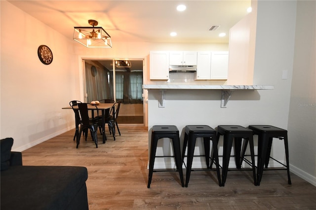 kitchen featuring a notable chandelier, wood-type flooring, a breakfast bar, decorative backsplash, and white cabinets