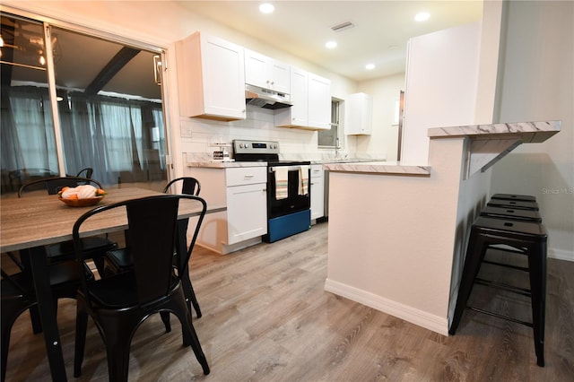 kitchen featuring light wood-type flooring, stainless steel electric range, a breakfast bar area, and white cabinets