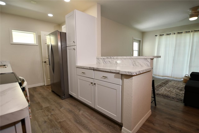 kitchen with dark hardwood / wood-style flooring, white cabinetry, kitchen peninsula, stainless steel refrigerator with ice dispenser, and a kitchen breakfast bar