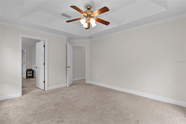 carpeted spare room with a tray ceiling, ceiling fan, and ornamental molding