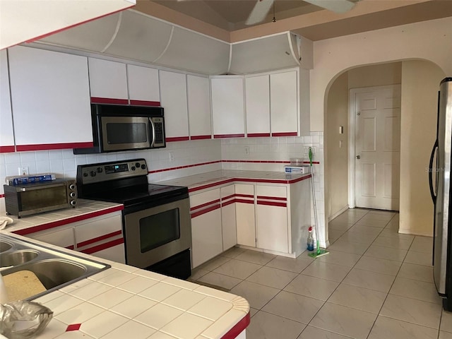 kitchen featuring light tile patterned floors, tile countertops, decorative backsplash, white cabinets, and appliances with stainless steel finishes