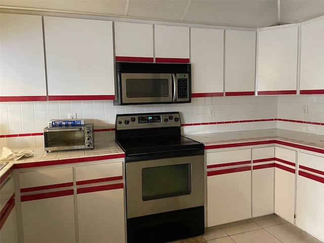 kitchen featuring tile countertops, white cabinets, decorative backsplash, appliances with stainless steel finishes, and light tile patterned flooring