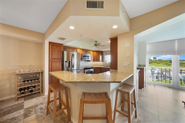 kitchen featuring appliances with stainless steel finishes, light stone countertops, kitchen peninsula, ceiling fan, and a breakfast bar