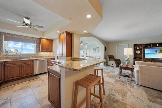 kitchen with dishwasher, ceiling fan, sink, and light stone countertops