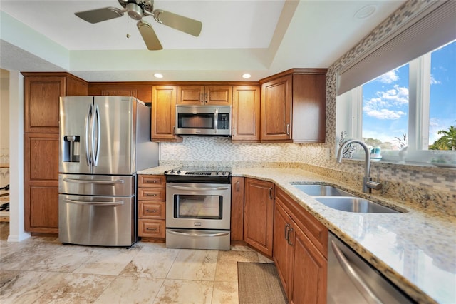 kitchen with backsplash, stainless steel appliances, sink, ceiling fan, and light stone countertops