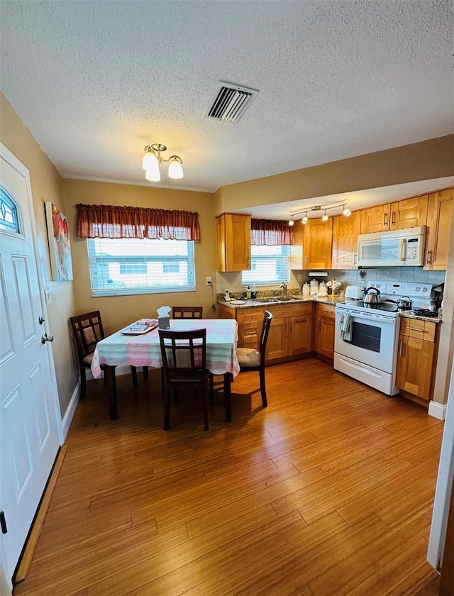 kitchen featuring light wood-style flooring, white appliances, a sink, visible vents, and tasteful backsplash