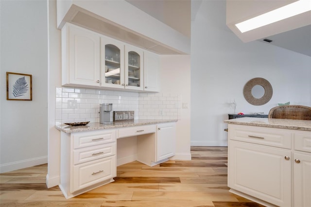 kitchen featuring built in desk, light stone countertops, white cabinetry, and light hardwood / wood-style flooring