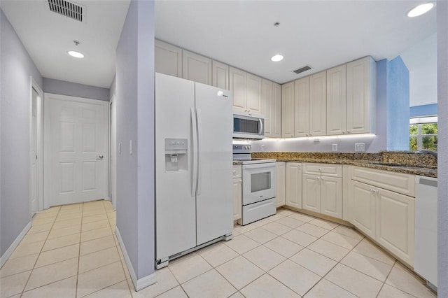 kitchen with dark stone countertops, sink, light tile patterned floors, and white appliances