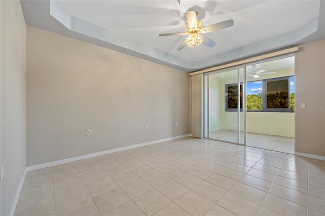 tiled empty room with a raised ceiling and ceiling fan