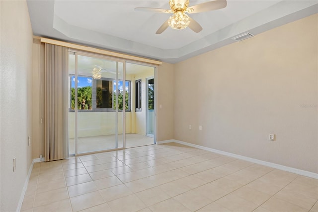 tiled empty room featuring ceiling fan and a raised ceiling