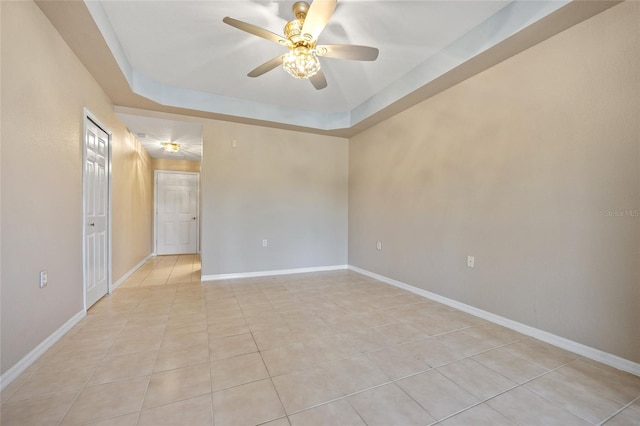 spare room featuring a tray ceiling, light tile patterned flooring, and ceiling fan