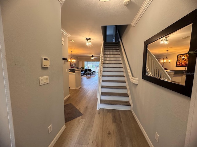 stairs featuring ceiling fan with notable chandelier, a textured ceiling, hardwood / wood-style flooring, and crown molding